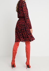 Black dress with red abstract pattern, fitted waist, long sleeves, and a flared skirt; paired with knee-high shiny red boots.