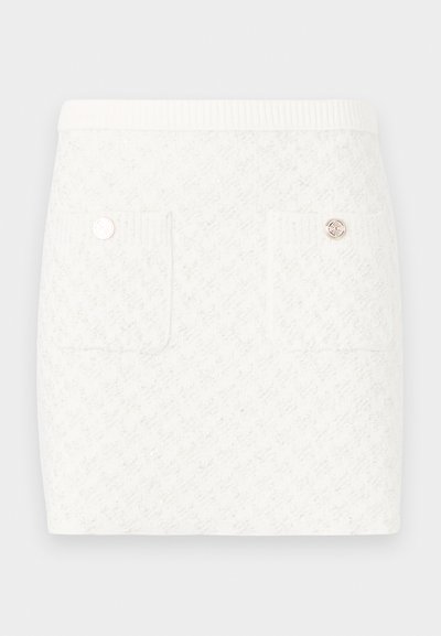 Jupe blanche courte avec un motif texturé, comportant deux poches avant et des boutons décoratifs en ton doré. Ceinture élastique pour plus de confort.