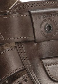 Zapato de cuero marrón con un diseño resistente, que cuenta con costuras de acento y una insignia de cuero de marca con un ojal de metal para el ajuste.