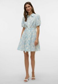 Abito a maniche corte, con bottoni, realizzato in un tessuto leggero con un motivo floreale blu. Presenta una vita cin cinata con una cintura coordinata.