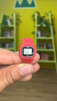 Montre digitale avec un bracelet en silicone rouge vif, un cadran carré noir et un affichage blanc indiquant l'heure. Conçue avec des accents texturés.