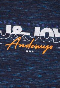 Tissu bleu marine présentant une texture chinée. Du texte imprimé en blanc et orange indique "J&JOY Andesuyo" avec un motif de design subtil.