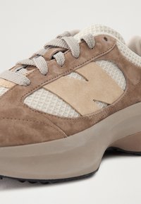 Baskets en daim beige et marron clair avec tissu en mesh, lacets beiges et semelle épaisse en caoutchouc, montrant un gros plan du côté et de la zone des orteils.