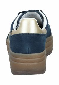 Mörkblå mockaskor med beige plattformssula och metallisk guldaccent på hälen, sedd bakifrån mot en vit bakgrund.