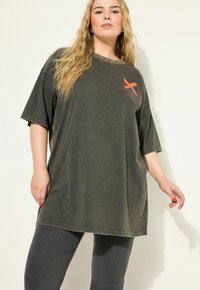 Übergroßes, dunkelgraues Baumwoll-T-Shirt mit kurzen Ärmeln, Rundhalsausschnitt und einem orangefarbenen Kreuzakzent auf der linken Brust. Lässige Passform.