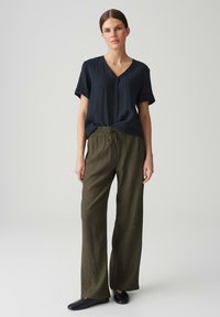 Top corto a maniche corte blu navy a V con finitura texturizzata, abbinato a pantaloni larghi olive green con cordino in vita. Scarpe nere senza lacci.