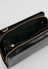 Portafoglio in pelle nera con chiusura a zip, dotato di hardware dorato, molteplici scomparti e una texture liscia sia all'interno che all'esterno.