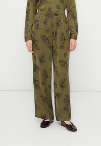 Pantaloni a palazzo verde oliva con vita con coulisse e stampa floreale scura, indossati con un top a maniche lunghe coordinato e ballerine rosso scuro.