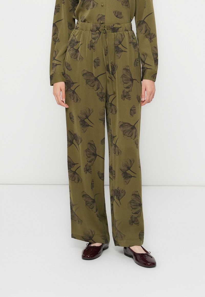 Pantaloni a palazzo verde oliva con vita con coulisse e stampa floreale scura, indossati con un top a maniche lunghe coordinato e ballerine rosso scuro.
