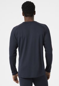 Camisa deportiva de manga larga en azul marino con un tejido texturizado, mangas raglán y acentos rojos en contraste a lo largo de los hombros y las mangas.