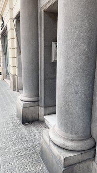 Colunas de pedra cinza com bases arredondadas, superfície texturizada e padrões subtis, emoldurando uma entrada recuada com um intercomunicador montado na parede.