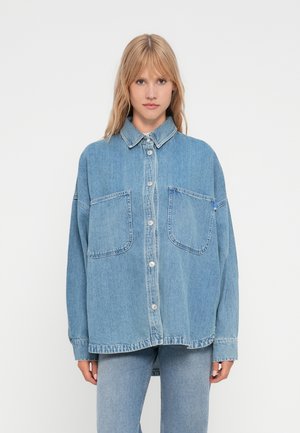 Lichtblauwe denim shirt met een kraag, twee grote voorzakken en knoopsluiting. Oversized pasvorm met zichtbare stiksels en een ontspannen ontwerp.