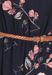 Flätad beige läderbälte som är fäst över en mörk tyg med rosa och grå blommönster.