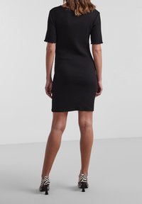 Abito nero a coste con maniche corte, caratterizzato da un orlo scallop. Abbinato a scarpe col tacco con stampa zebra. Tessuto liscio, design aderente.