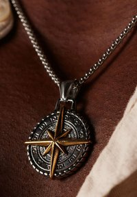 Zilveren ketting met een ronde hanger waarin een gouden kompasster is verwerkt, met een gestructureerde zilveren achtergrond en gegraveerde details rond de rand.