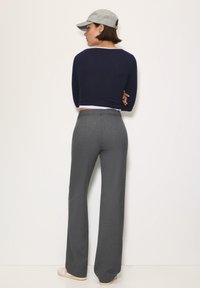 Marineblauwe cropped trui, grijze nauwsluitende broek en een grijze pet; de outfit heeft een gladde textuur en een getailleerd ontwerp, met een open rugdetail.