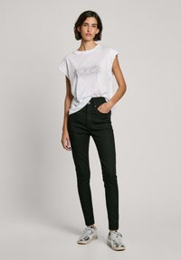Bílý tričko s krátkým rukávem s metalickým potiskem "PEPE JEANS", v kombinaci s černými skinny džínami s vysokým pasem a stříbrnými teniskami. Jednoduchý, ležérní vzhled.