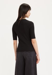 Haut noir à manches courtes en coton lisse, avec une silhouette ajustée et un col rond, associé à un jean large foncé.