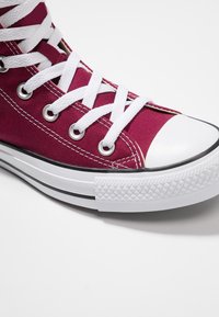 Burgunderfarbene High-Top-Sneaker aus Canvas mit weißen Schnürsenkeln, Gummikappen und einer schwarz-weißen Gummisohle mit strukturierten Mustern.