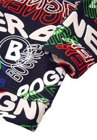 Tela de algodón con un fondo marino y texto y logotipos multicolores en blanco, rojo, verde y azul. Textura suave con borde plegado.