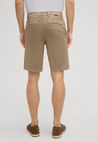 Pantalones cortos beige hechos de una tela ligera con un corte recto, que cuentan con dos bolsillos traseros y dobladillos acabados. Llevados con zapatos casuales marrones.