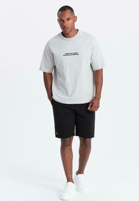 T-shirt grigia con testo nero, abbinata a pantaloni corti neri texturizzati. Sneakers bianche completano l'outfit. Design semplice e casual.