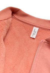 Chaqueta de forro polar rosa con cuello acanalado, cierre de cremallera en la parte delantera y etiqueta interior. La tela parece suave y con una textura lisa.