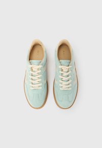 Világoskék velúr sportcipőpár krémszínű fűzőkkel és részletekkel, barna gumitalpakkal, felülről fehér háttéren nézve.