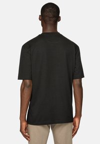 Musta lyhythihainen T-paita, joka on valmistettu puuvillasta. Sillä on pyöreä kaula-aukko ja väljä malli. Sileä pinta, jossa on ommeltu helma ja minimaalinen yksityiskohtaisuus.