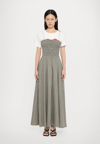 Rochie maxi cu bustă striată în verde măsliniu și dungi albe, având o fustă lungă și fluidă. Asortată cu un tricou alb și sandale negre.