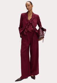Bordeaux pak met een gerimpeld blouse, een op maat gemaakte blazer met knopen,wijd-pijperige broek en puntige schoenen met oogjes.