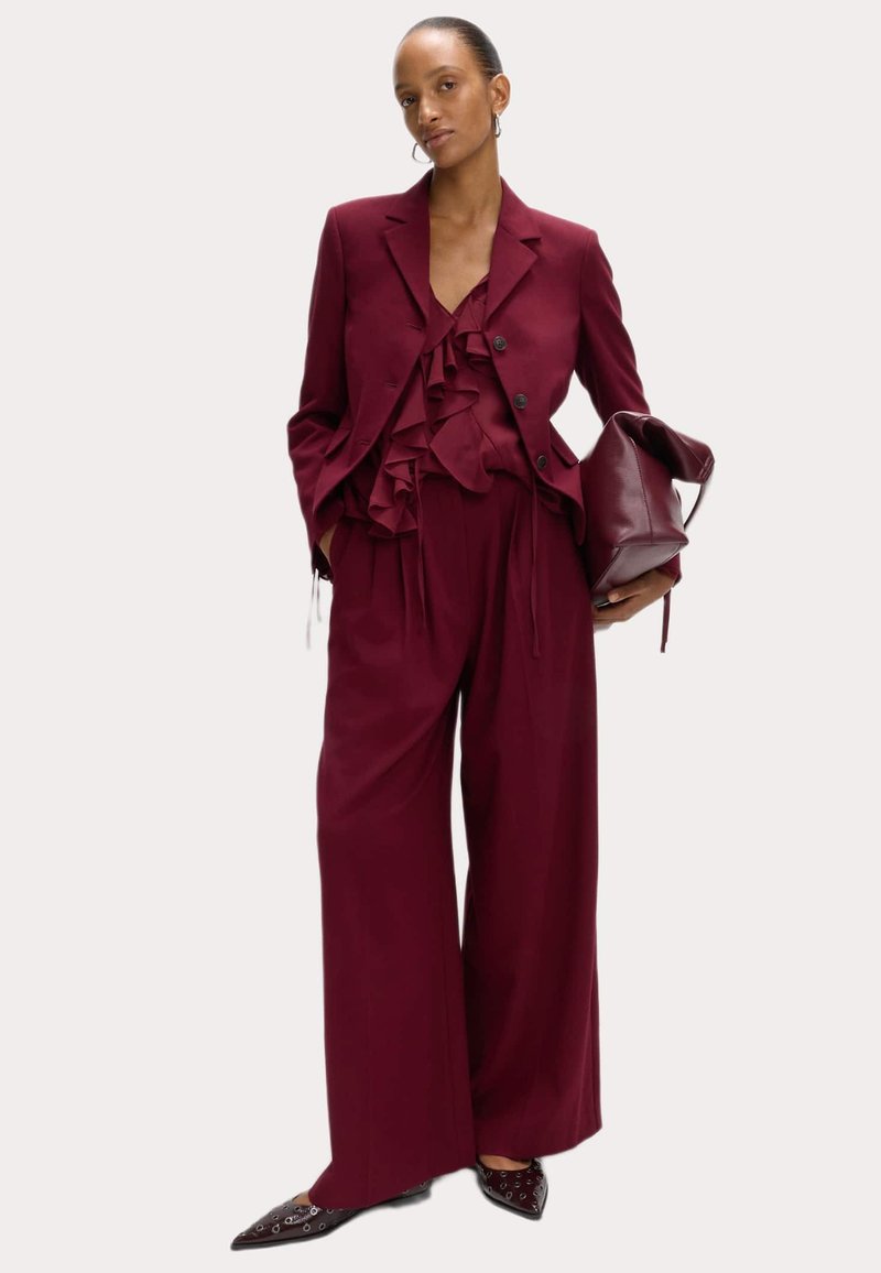 Bordeaux pak met een gerimpeld blouse, een op maat gemaakte blazer met knopen,wijd-pijperige broek en puntige schoenen met oogjes.