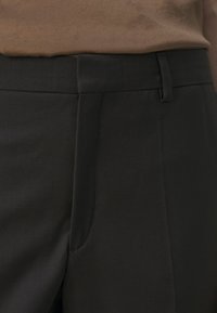 Pantalon noir sur mesure avec une texture lisse, doté d'un devant plat et d'une coupe slim. Comprend une poche latérale, avec une finition légèrement brillante.