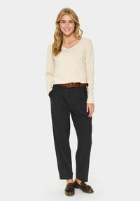 Bēša garām piedurknēm V-veida kakla izgriezuma krekls, tumši pelēki krokoti bikses, brūns ādas josta un tumši apavi ar tekstūrētu apdari.