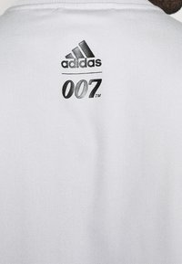 White athletic shirt with a textured fabric. Features black Adidas logo and "007" graphic printed on the back. Simple design and minimalistic style.