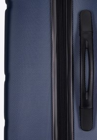 Valigia rigida di colore blu navy con superficie testurizzata, caratterizzata da una cerniera nera e una maniglia. Design minimalista, forma compatta, materiale resistente.