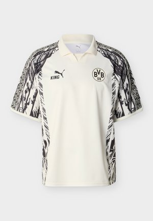 Hvid polo med sorte abstrakte mønstre på ærmerne, Borussia Dortmund BVB 09-logo på brystet og Puma-logo med teksten "KING".