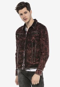 Rote, distressed Jeansjacke mit Nieten, ausgestattet mit zwei Brusttaschen, einer Knopfverschlüsse und einem schwarzen Kragen. Texturiertes Material mit detailreicher Nahtführung.