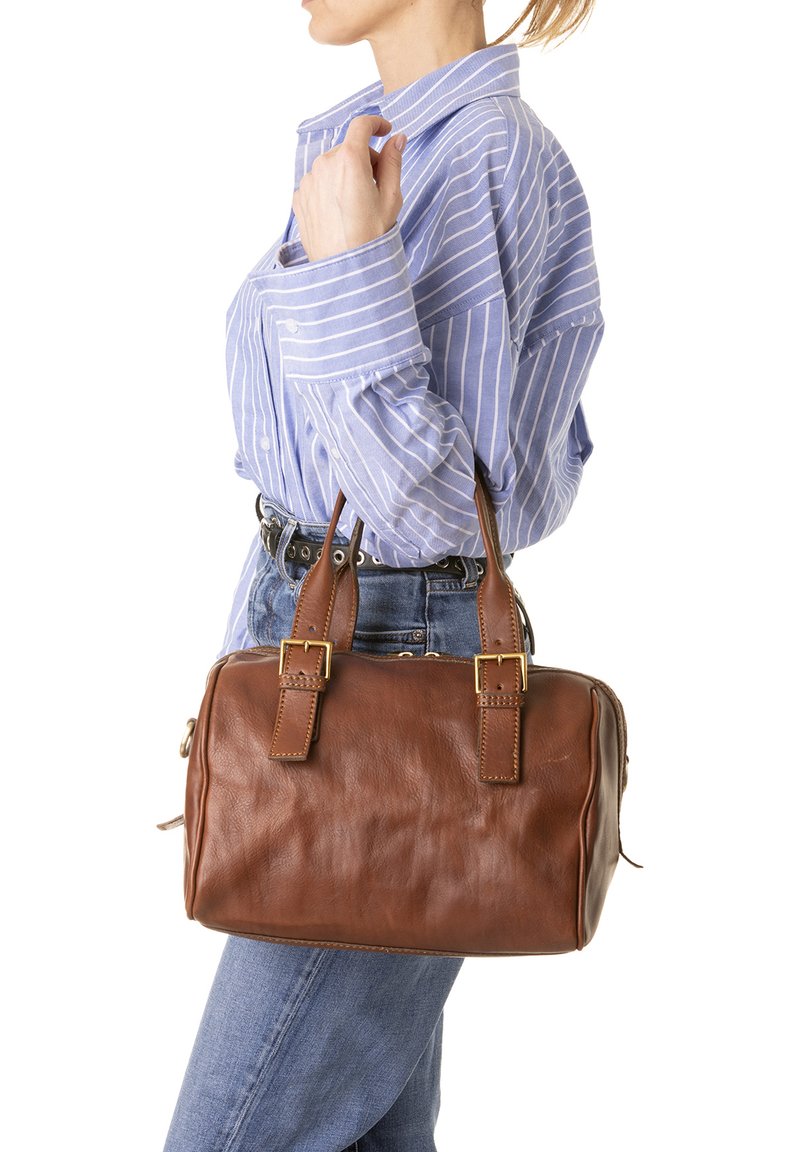 Borsa a mano in pelle marrone con hardware dorato, forma rettangolare, doppio manico e dettagli di cucitura visibili. Indossata insieme a una camicia a righe blu.