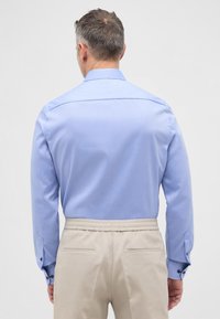 Hellblaues langärmliges Hemd mit geradem Kragen, knöpfbaren Manschetten und glatter Textur, kombiniert mit beigen Hosen mit elastischem Bund.