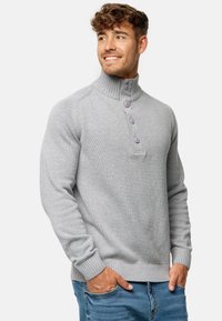 Suéter gris de punto con cuello alto, que presenta cuatro botones morados. Puños y dobladillo acanalados, que muestran un diseño de tela texturizada.