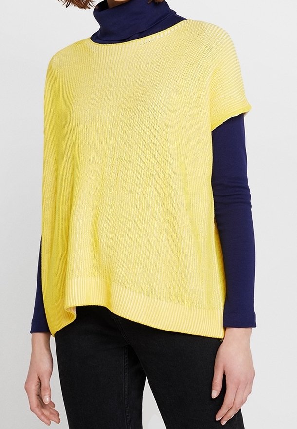 Žlutý žebrovaný pletený svetr s krátkými rukávy, vrstvený přes námořnický rolák. Spodní lem má mírný oblouk a texturovaný povrch.