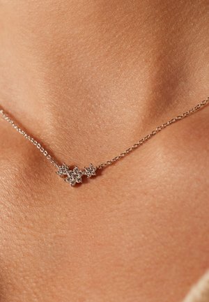 Delicate silver chain necklace with three small flower-shaped diamond clusters resting on a person's collarbone.