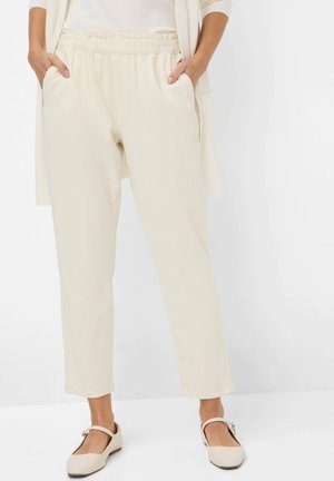 Pantalons légers couleur crème avec une taille élastique, des poches latérales et des jambes fuselées, assortis de chaussures à brides simples.