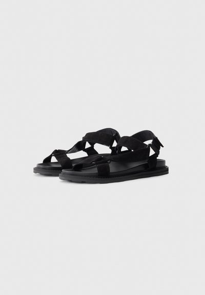 Sandale negre din suede cu multiple curele, suprafață texturată, talpă plană din cauciuc și design cu vârful deschis, dotate cu sistem de închidere ajustabil.
