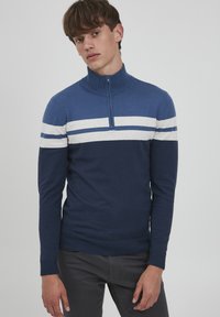 Blauer und marine gestreifter Reißverschluss-Pullover mit hohem Kragen und langen Ärmeln, aus weichem Stoff mit gerippten Bündchen und Saum.