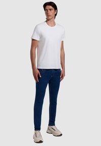 T-shirt bianco a maniche corte abbinato a jeans blu slim-fit e sneakers bianche da ginnastica. Design semplice, scollatura rotonda e texture liscia.