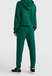 Haut à capuche vert court avec capuche et joggers assortis. Tissu lisse, poignets côtelés, taille élastique, et baskets noires avec semelles blanches.