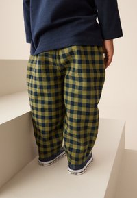 Zeleno in mornarsko modro karo hlače z ohlapno prileganjem, kombinirane z mornarsko modrimi supergami. Material ima mehko teksturo in vidni tartan vzorec.