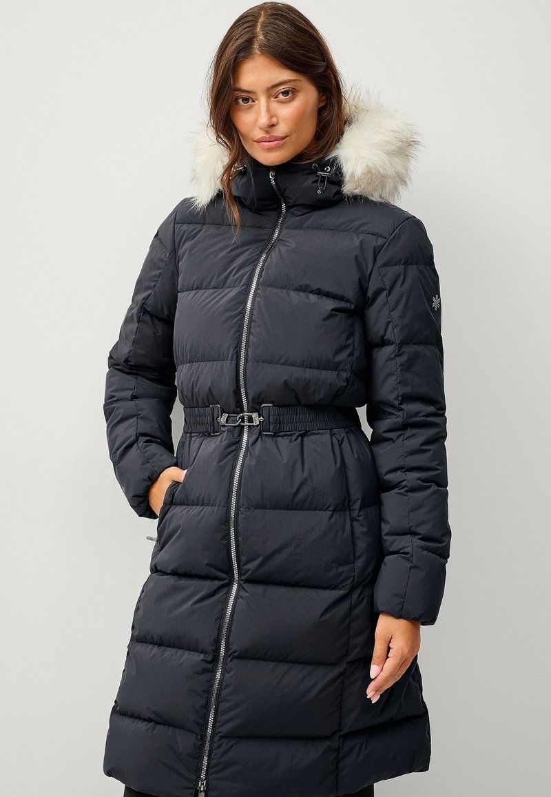 Sort pufferjakke med en faux fur hætte, bælte i taljen, lynlås foran og quiltet design. Har to sidelommer og elastiske manchetter.